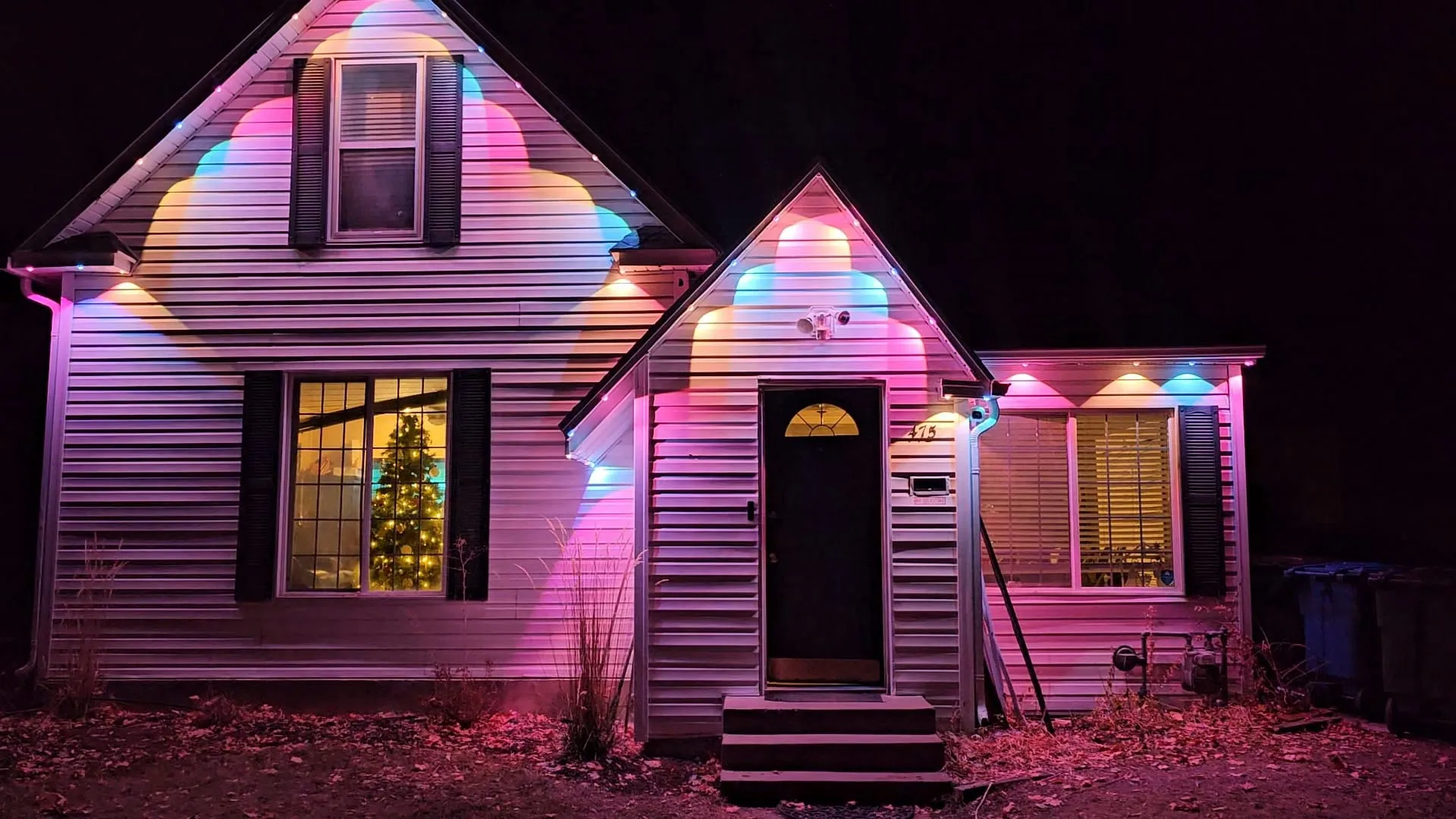 White cottage with pink, purple, and cyan birthday-scene permanent lighting